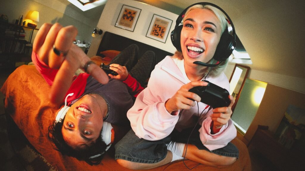 Dos personas jugando videojuegos con audífonos JBL Quantum 250 frente a una pantalla iluminada