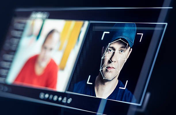 Pantalla de monitor que muestra un sistema de reconocimiento facial con mallas geométricas analizando el rostro de un hombre con gorra.